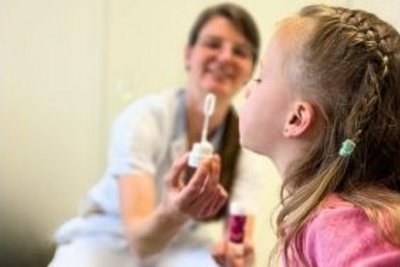 Mädchen sitzt am Schoss der Mama und bläst Seifenblasen