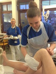 eine Schülerin serviert ein Tablett ab, eine weitere wäscht einem Patienten das Bein