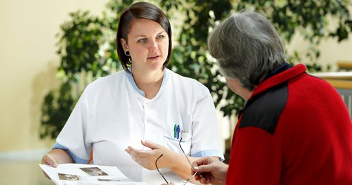 Eine Mitarbeiterin hält ein Fotoalbum und spricht mit einer Patientin