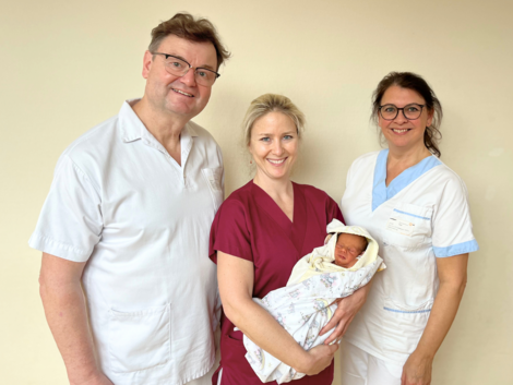 Arzt neben Hebamme und Stationsleiterin, Hebamme hält Baby im Arm