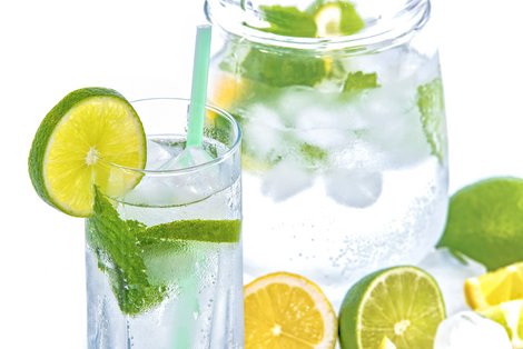 Glas und Krug mit Wasser, Eiswürfel und Limettenscheiben
