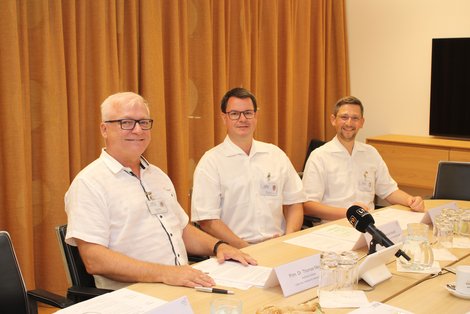 Drei Ärzte sitzen an einem Tisch - Pressekonferenzsituation