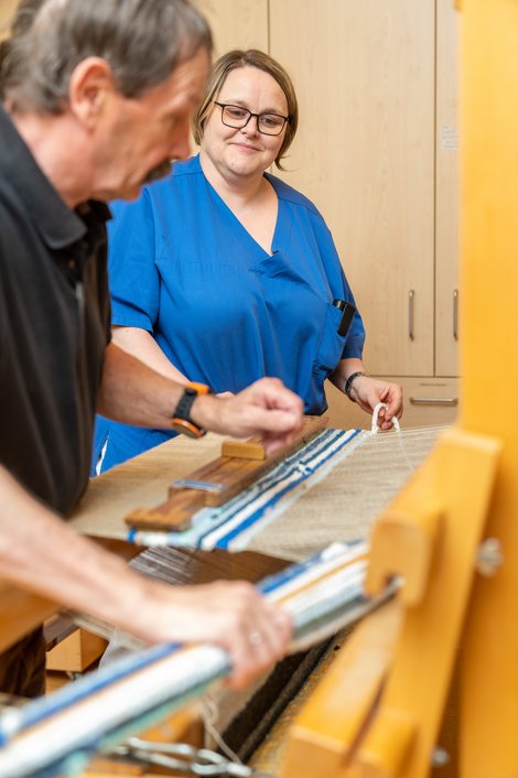 Hier arbeitet Martina Ruhmer, Diplom-Sozialbetreuerin mit Schwerpunkt Behindertenarbeit und Behindertenbegleitung, mit Bewohner Fritz Bauernfeind am Webstuhl in der Kreativwerkstatt des Schlosses.
