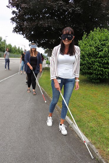 Auszubildende mit Augenbinde und Blindenstock auf dem Gehsteig