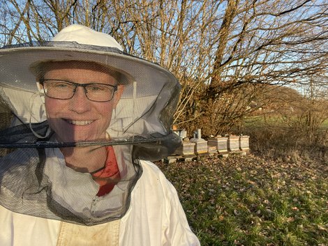 Selfie von Ruth Bahmann im Imker-Anzug steht vor Bienenstöcken