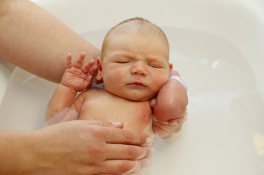 Neugeborenes wird in der Badewanne gewaschen.