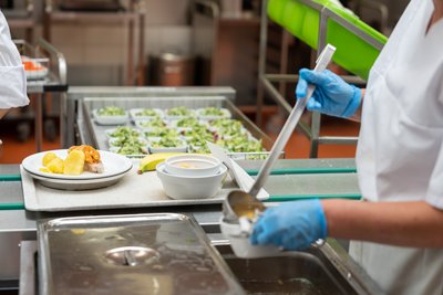 Mitarbeiterin in der Küche gibt Suppe in Schalen