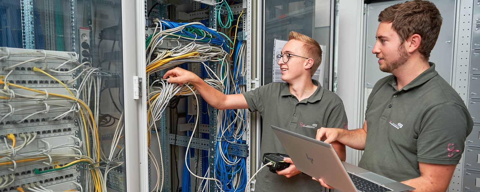 Zwei MIT-Mitarbeiter schauen sich Kabeln im Büro-Serverraum an.