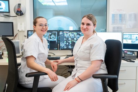 zwei Mitarbeiterinnen vor Bildschirmen und MRT im Hintergrund