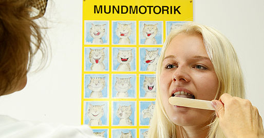 Logopädin hält Patientin eine Holzspatel an die Zunge