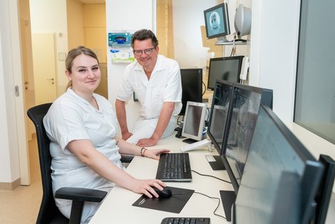 Primar und Mitarbeiterin gemeinsam vor einer Reihe von Bildschirmen