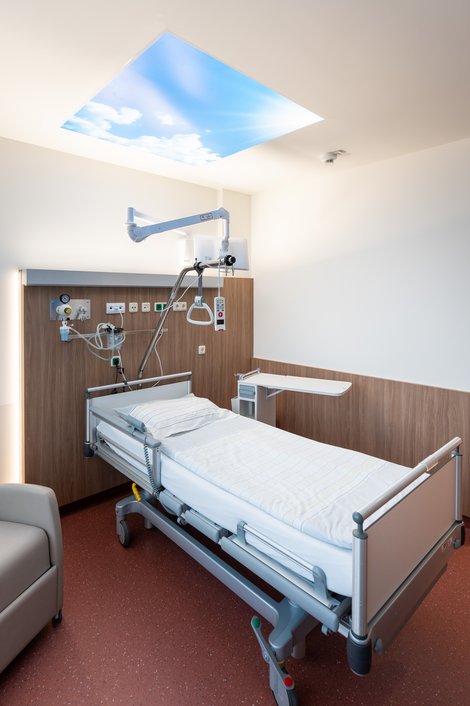 Krankenzimmer mit Bett und beleuchtetem Deckenbild