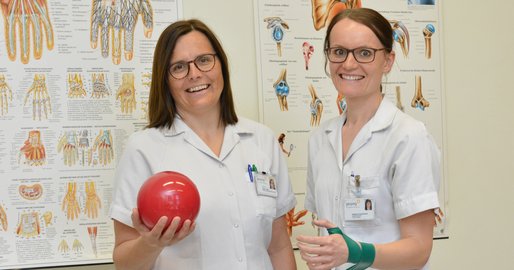 Zwei Mitarbeiterinnen des Ergoteams halten einen Ball und einen Theraband