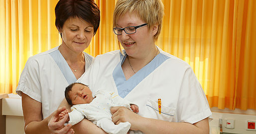 Zwei Mitarbeiterinnen mit einem Baby in der Hand