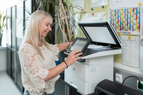 Sylvia Hollnsteiner in ihrem Büro schaut beim Drucken lächelnd in die Kamera