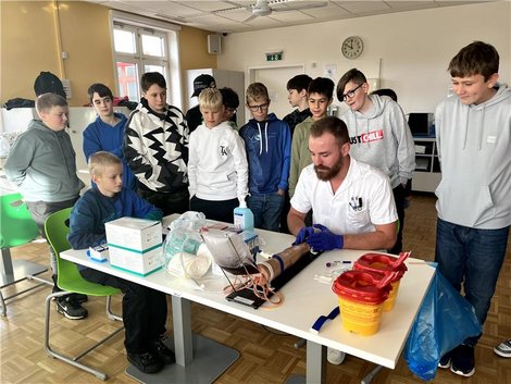 Martin Binder erklärt im Rahmen einer Informationsveranstaltung interessierten jungen SchülerInnen die Blutabnahme