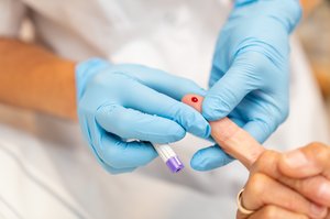 Hände mit Handschuhen bei einer Blutabnahme