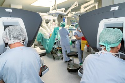 Chirurgen an den Konsolen und im Hintergrund der OP-Roboter im Einsatz