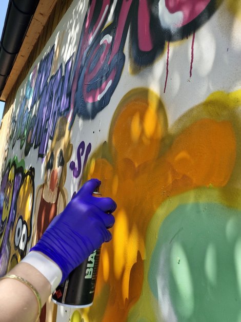 Hand mit Handschuh beim Sprühen eines Grafitti