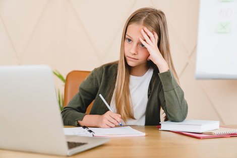 Kind sitzt vor Laptop und hält sich den Kopf