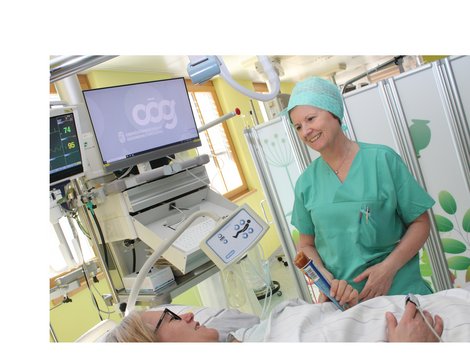 Mitarbeiterin im grünen OP-Gewand gibt Patientin im Krankenbett ein Eis