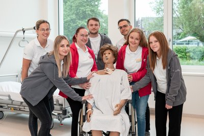 Gruppenfoto Auszubildende mit Simulationspuppe im Rollstuhl