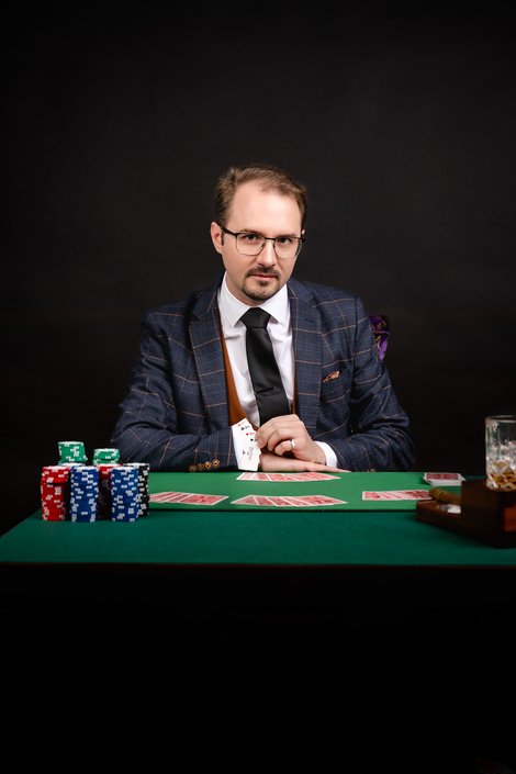 Zauberkünstler Harald Brunner („Harry Fontaine“) sitzt an einem Spieltisch mit Pokerchips und Karten und führt einen klassischen Kartentrick in ruhiger, stilvoller Studioumgebung vor.