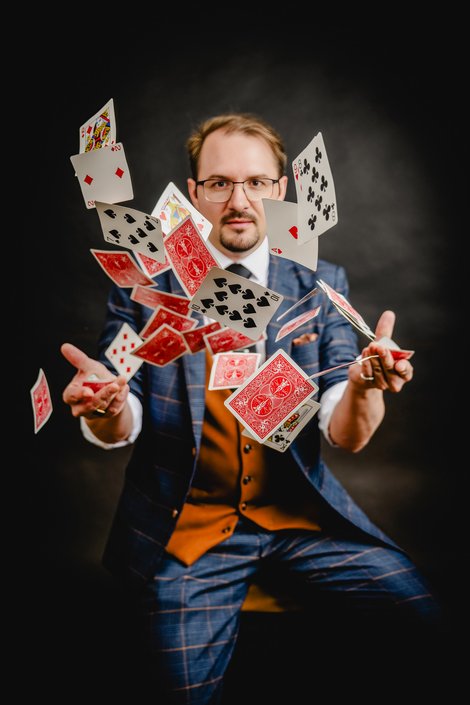 Zauberkünstler Harald Brunner („Harry Fontaine“) lässt mehrere Spielkarten effektvoll durch die Luft wirbeln und präsentiert eine dynamische Kartenillusion vor dunklem Hintergrund.