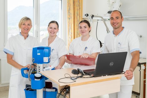 Vier Pflegekräfte im Krankenzimmer mit Laptop und medizinischem Gerät