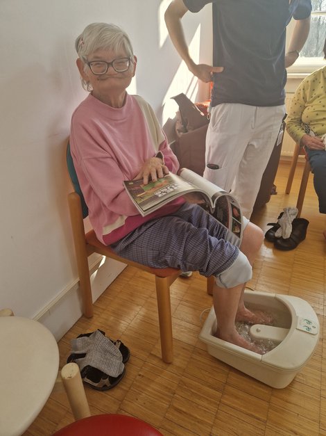 Bewohnerin bekommt Fußbad und liest Zeitschrift