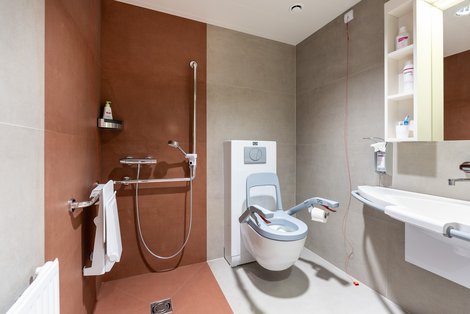 Badezimmer mit Waschbecken, höhenverstellbarem WC und begehbarer Dusche