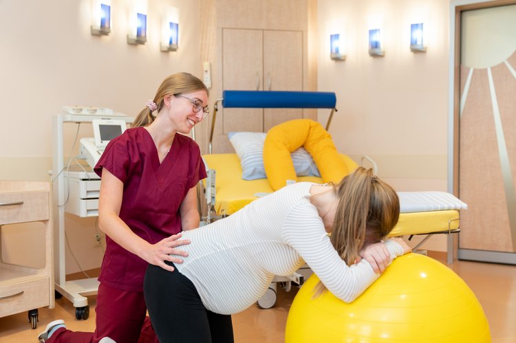 Hebamme unterstützt Schwangere die sich auf einem Gymnastikball anlehnt