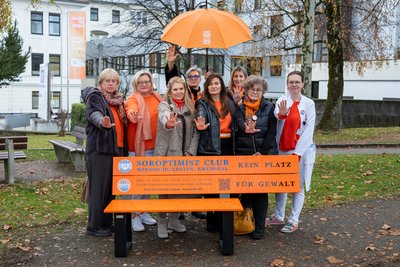 Gruppenfoto Frauen mit orangenem Schirm hinter orangener Parkbank