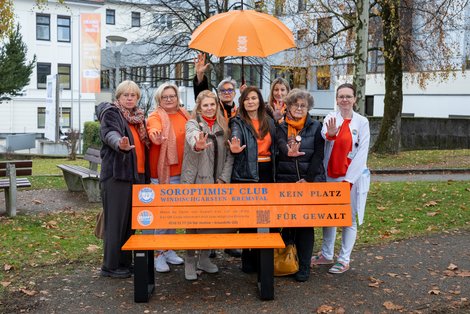 Gruppenfoto Frauen mit orangenem Schirm hinter orangener Parkbank