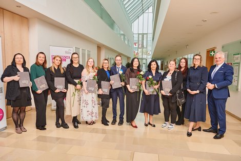 Gruppenfoto AbsolventInnen mit Diplom und Blume in der Hand mit Gratulanten