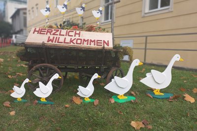 Heuwagen mit Schild: Herzlich Willkommen, davor Aufsteller in Form von Gänsen