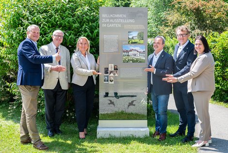 Gruppenbild und alle zeigen auf die Stele der Ausstellung