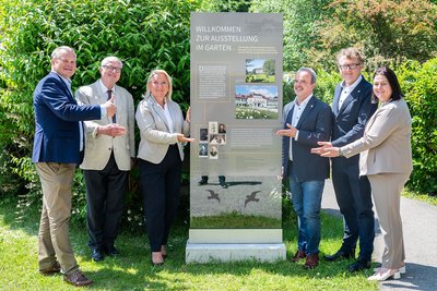 Gruppenbild und alle zeigen auf die Stele der Ausstellung