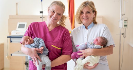 Zwei Mitarbeiterinnen halten zwei Neugeborene 