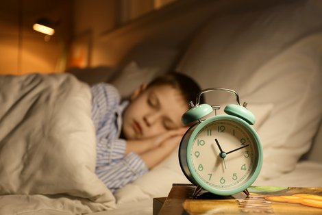 Kind schläft im Bett, im Vordergrund steht ein Wecker