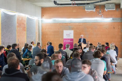 Gäste sitzen an Biertischen im Rohbach, vorne spricht GF Lehner