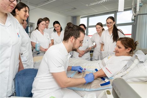 Ausbildungssituation: PflegeschülerInnen rund um Krankenbett beim Blutabnehmen