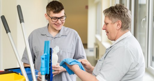 Lehrling Reinigungstechnik vor einem Putzwagen mit einer Kollegin