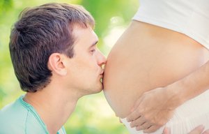 Mann küsst schwangere Frau auf dem Bauch