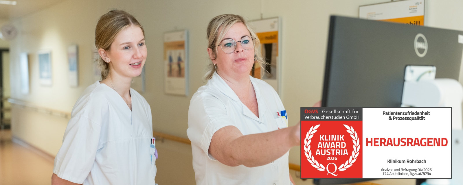 Zwei Mitarbeitende der Pflege stehen vor einem Bildschirm auf einer Station des Klinikum Rohrbach; im Bild ist der Klinik Award Austria – Herausragend eingeblendet.