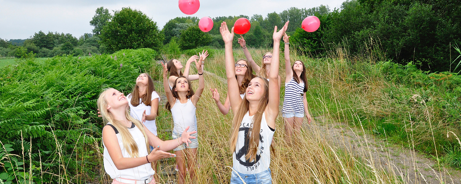 Acht Mädchen spielen mit roten Ballons im Feld 