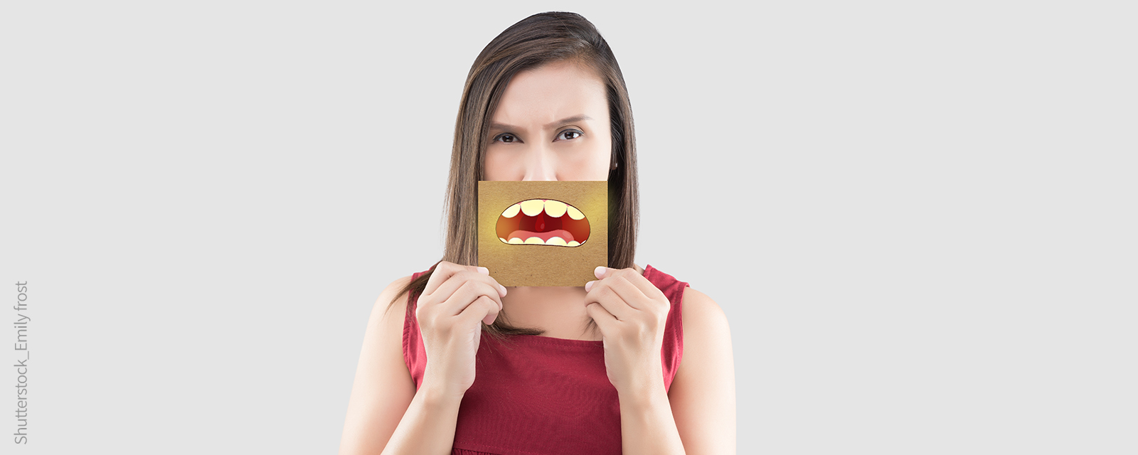 Frau hält ein Bild mit einem Mund mit gelben Zähnen vor das Gesicht