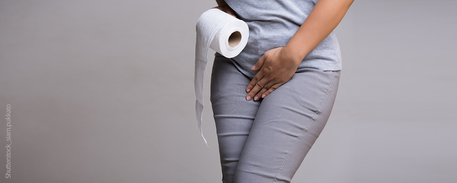 Frau mit Toilettenpapier in der Hand verschränkt die Beine und greift zum Intinbereich
