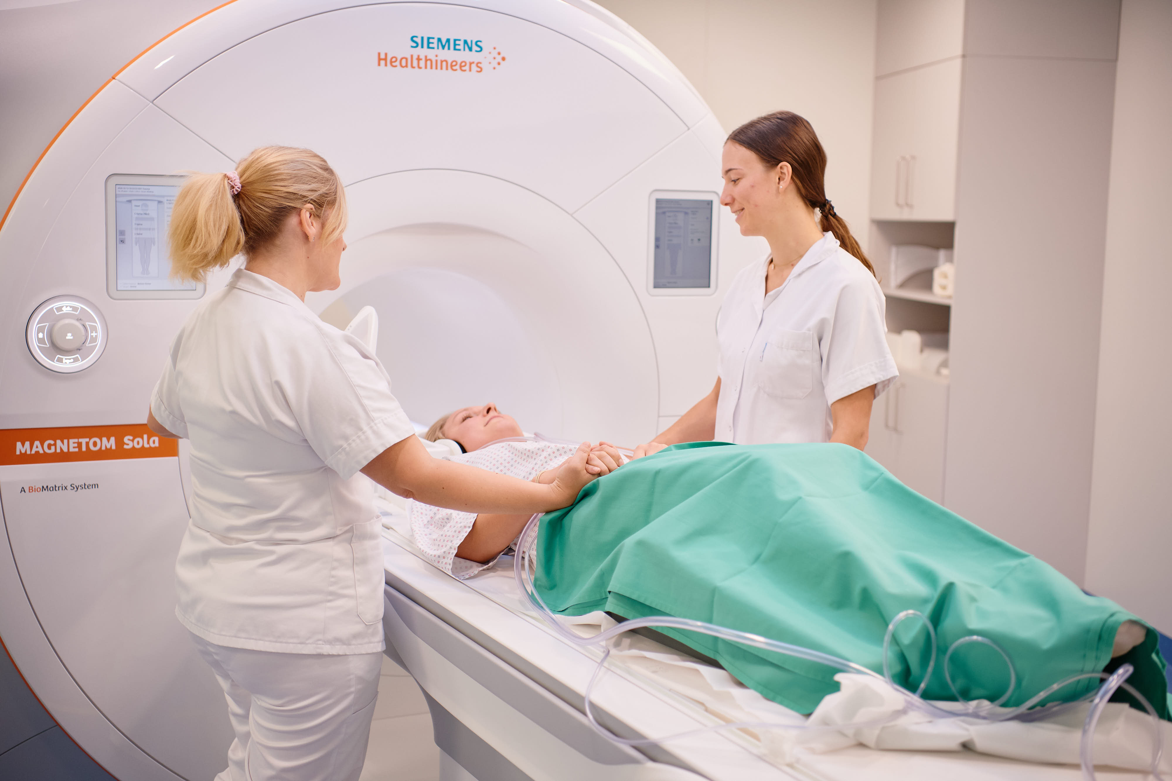 MRT-Untersuchung: Patientin liegt auf Liege, zwei Radiologiefachangestellte im Gespräch